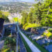 A long outdoor ramp descending a forested hillside, with metal rails and green turf, overlooking a town in the valley.
