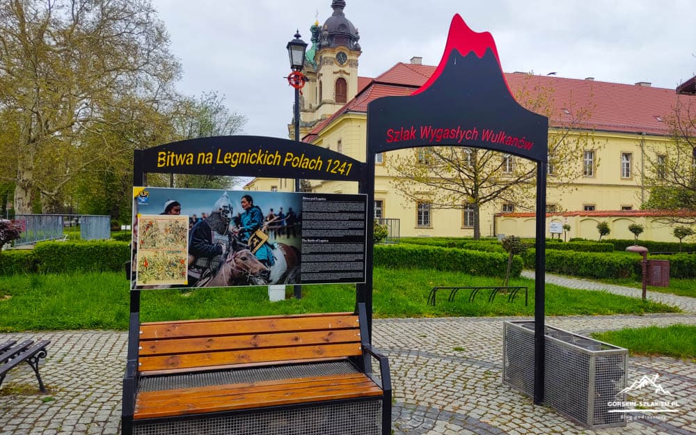 Park information display and bench; signs read 'Bitwa na Legnickich Polach 1241' and 'Szlak Wygasłych Wulkanów'.