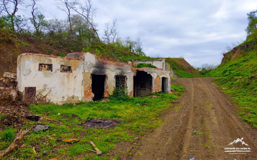 Abandoned brick and concrete buildings along a muddy dirt road in a hilly, grassy landscape.