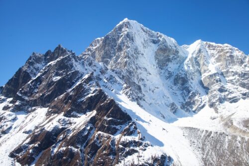 Snow-covered jagged mountain peaks rise against a bright blue sky in a high-alpine landscape.