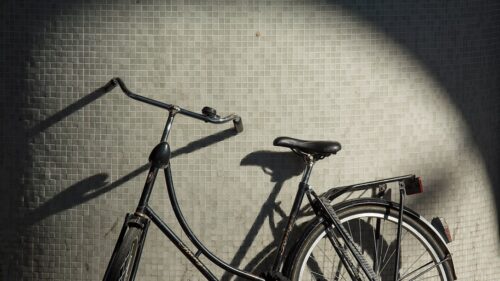Black vintage bicycle parked against a gray tiled wall with a spotlight circle of light on the wall behind it.