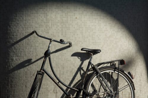 Black vintage bicycle parked against a gray tiled wall with a spotlight circle of light on the wall behind it.