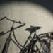 Black vintage bicycle parked against a gray tiled wall with a spotlight circle of light on the wall behind it.