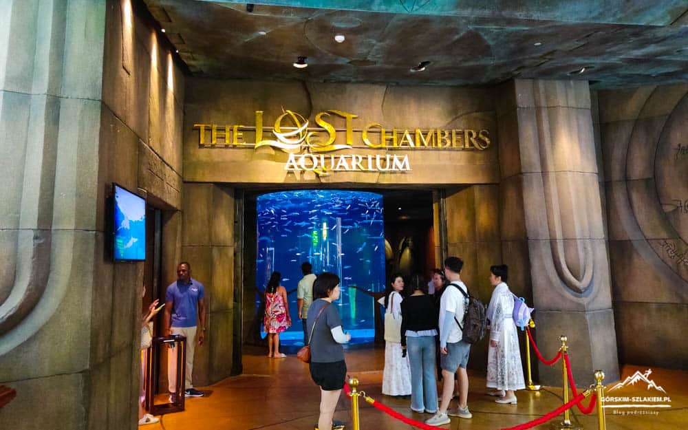 Entrance to The Lost Chambers Aquarium with visitors near a red rope barrier and a blue-lit lobby beyond.