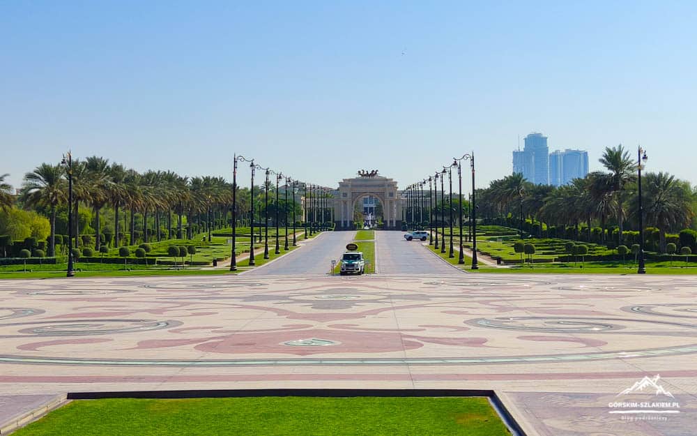 Wide view of a formal park and plaza with palm-lined avenues, leading to an ornate gateway at the far end.