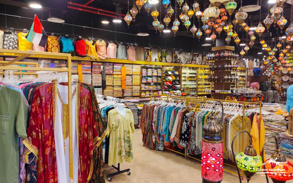 Vibrant ethnic clothing shop with racks of colorful dresses and folded fabrics, lanterns hanging from the ceiling in a well-lit boutique.