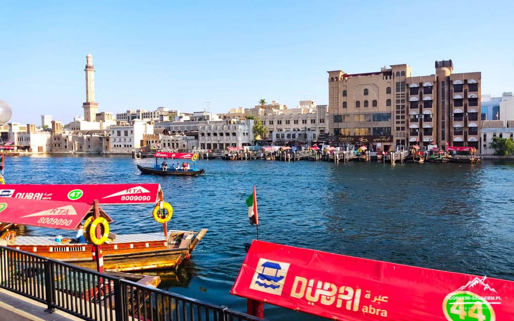 Dubai Creek waterfront with colorful abra boats and historic-style buildings along the water.