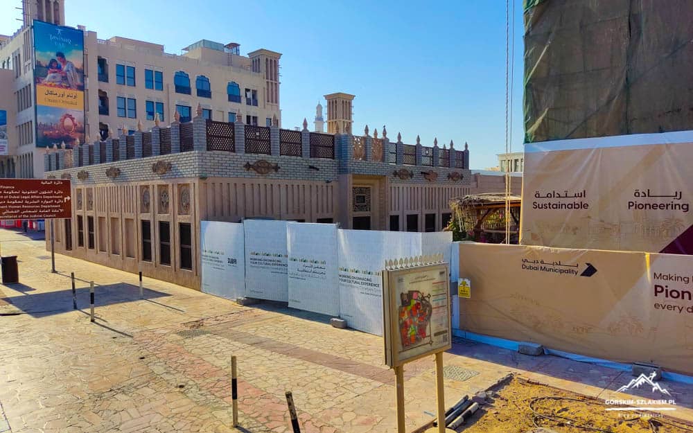Construction site with a beige ornate wall, blue banners and signage about Dubai Municipality and sustainability against a clear blue sky