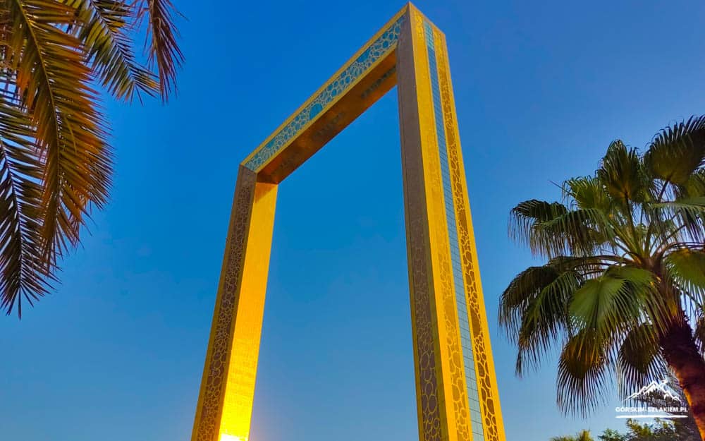 Golden decorative arch frame reaching into a clear blue sky, with palm trees on both sides.