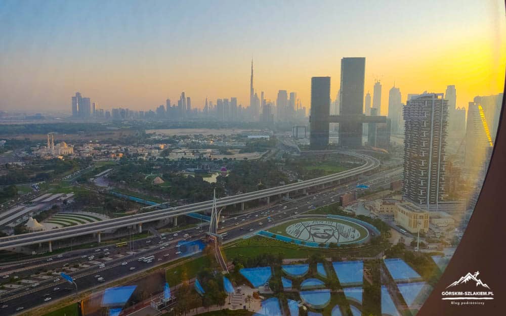 Dubai skyline at sunrise with tall buildings and a network of elevated roads in the foreground, viewed from a window