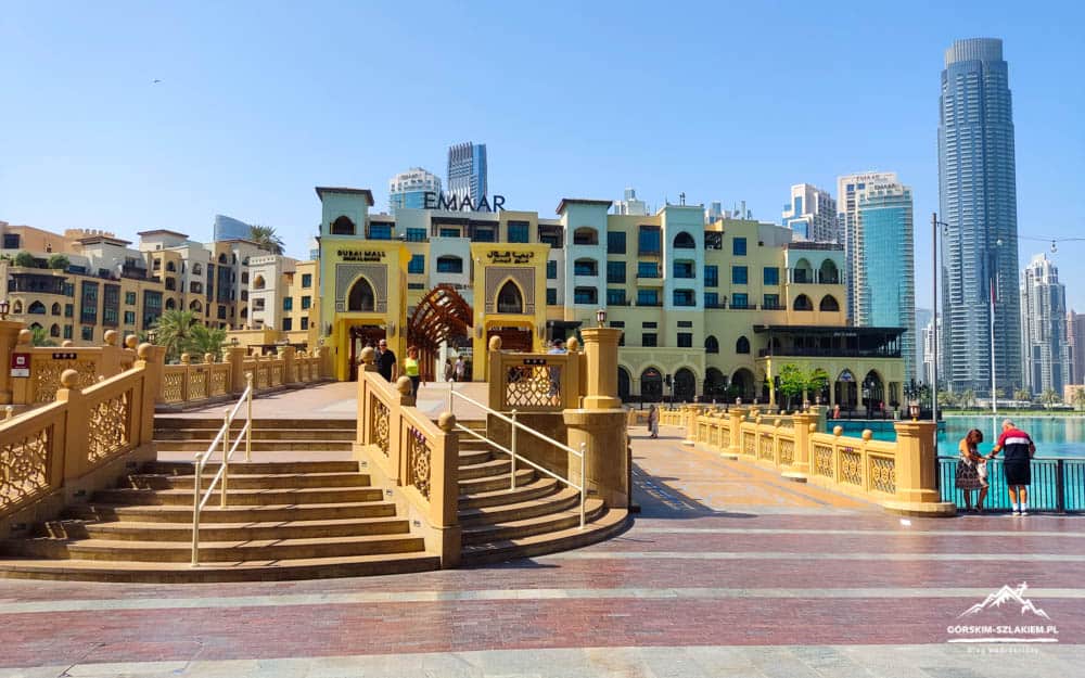 Promenade with ornate yellow railings and wide stairs, pastel buildings, and a canal with skyscrapers in the background. - Informative and concise idea of location and scenery.