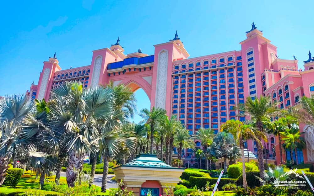Large pink resort hotel with an arched entrance, surrounded by palm trees under a bright blue sky.