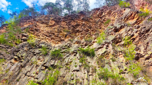 Cliff of hexagonal basalt columns with sparse greenery and a blue sky above.