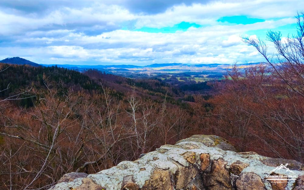 View from a rocky overlook over bare trees and a distant valley under cloudy skies in a wintry landscape.
