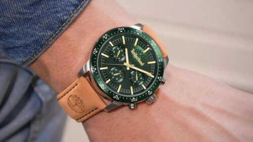 Green dial chronograph watch with a tan leather strap on a wrist, denim sleeve in the background.
