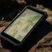 Smartphone displaying a topographic map with a blue navigation arrow on a rocky surface.