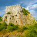 Large rocky limestone hill rising above green shrubland under a partly cloudy blue sky.