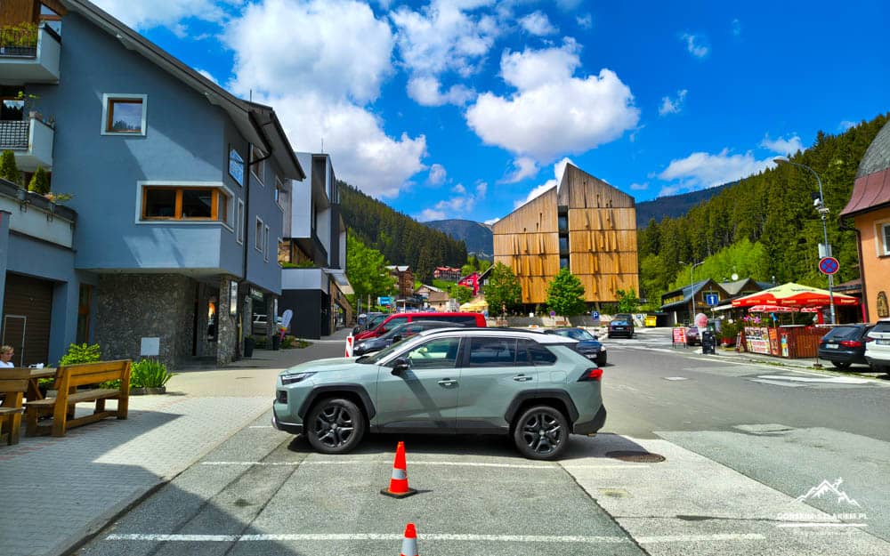 Grey SUV parked across a crosswalk in a mountain-town street with orange traffic cones nearby