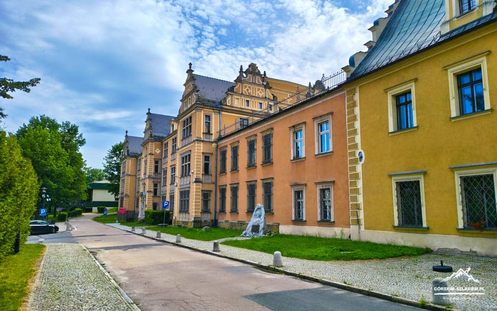 Historic European street with pastel orange and yellow townhouses, a cobblestone path, and a small stone sculpture in front.