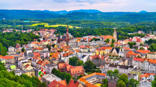 Aerial view of a European town with red and orange rooftops set among green hills and trees:**