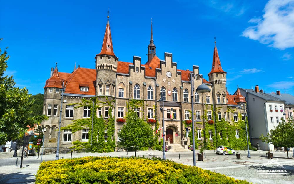 Historic brick town hall with red-tiled roofs, ivy-covered walls, and two corner towers against a blue sky.