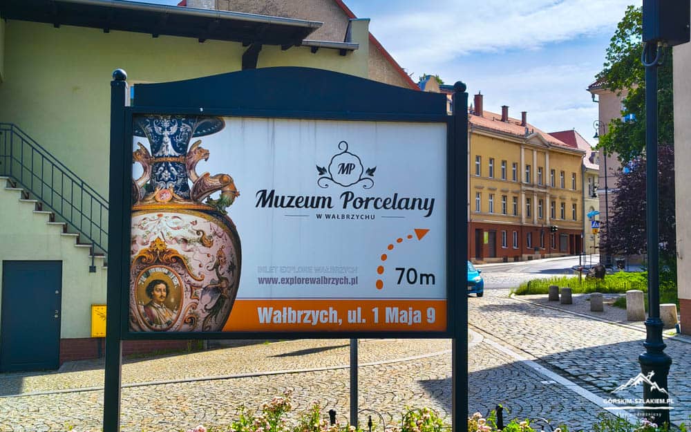 Signboard advertising the Porcelain Museum in Wałbrzych, with an orange address bar and a 70 m arrow toward the street.
