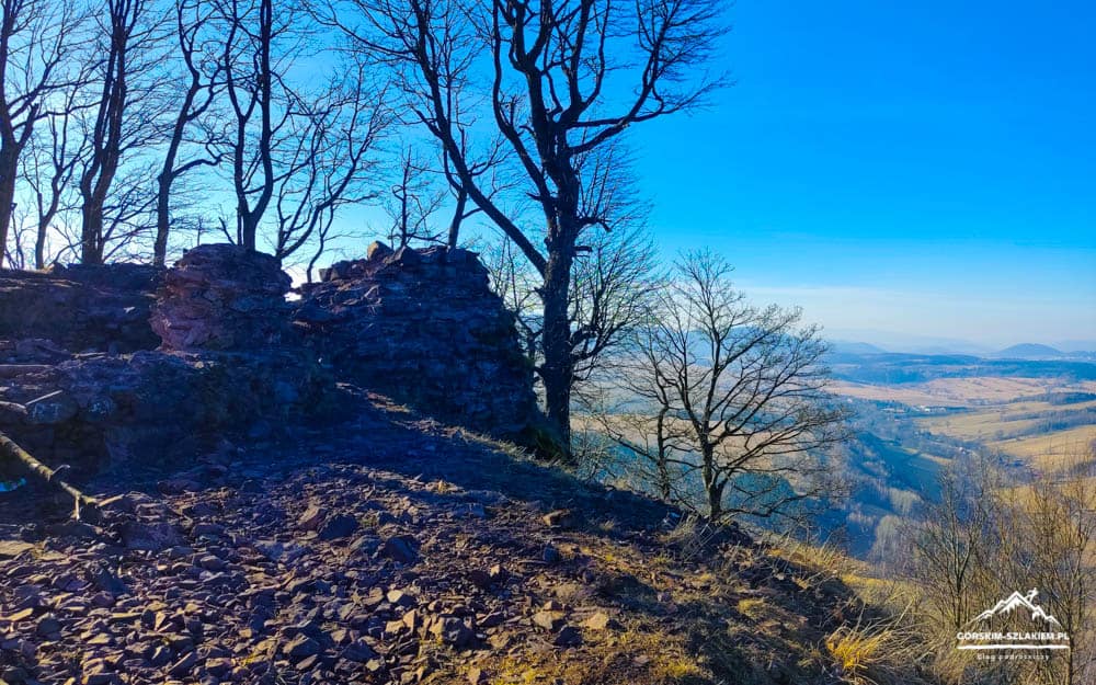 Rocky hilltop with crumbling stone walls, bare trees, and a wide valley below on a clear day.