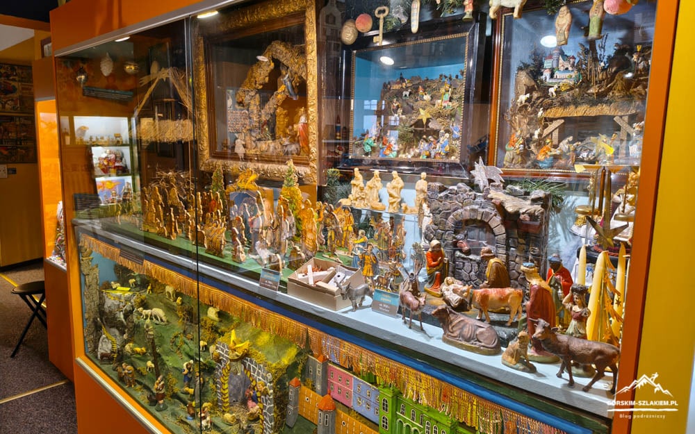 Glass display case in a shop window filled with colorful miniature nativity scenes and village dioramas.