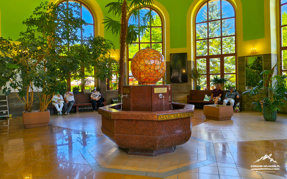 Lobby atrium with a circular granite fountain and a mosaic orange globe on top, surrounded by green walls and arched windows.