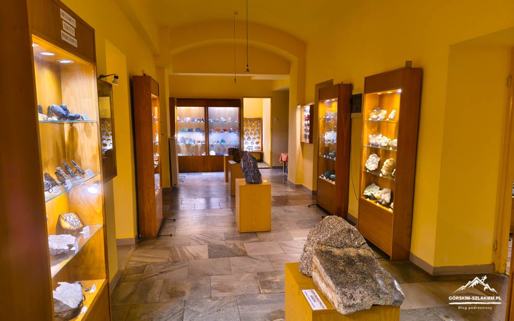 Interior of a mineral museum: yellow-walled gallery with glass display cases of rocks and minerals, and a large rock on a pedestal in the center.