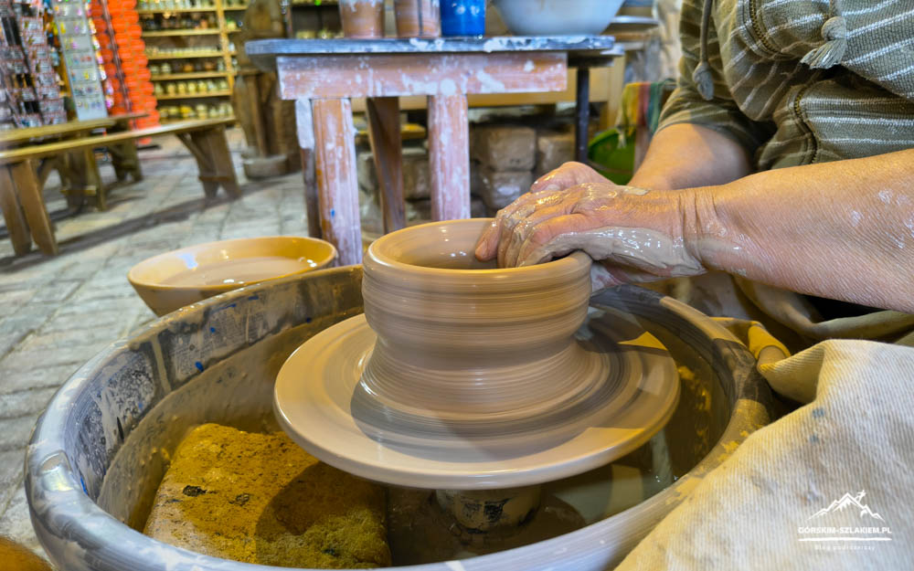 Potter shaping a clay vase on a spinning pottery wheel with muddy hands in a studio workshop.