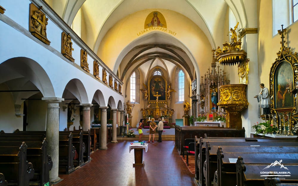 Interior of a church with vaulted arches, wooden pews, and a gilded altarpiece at the far end.