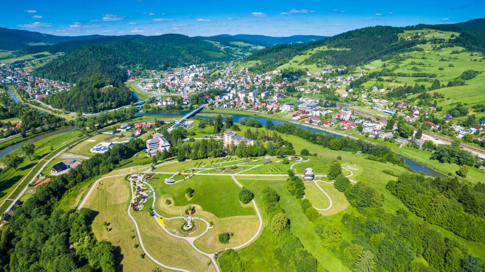 Aerial view of a valley town with a winding river, bridges, and green hills surrounding a dense neighborhood scene in the center and background.