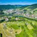 Aerial view of a valley town with a winding river, bridges, and green hills surrounding a dense neighborhood scene in the center and background.