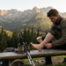 Hiker sits on a wooden bench in the mountains, wrapping his ankle with a bandage beside boots and trekking poles.